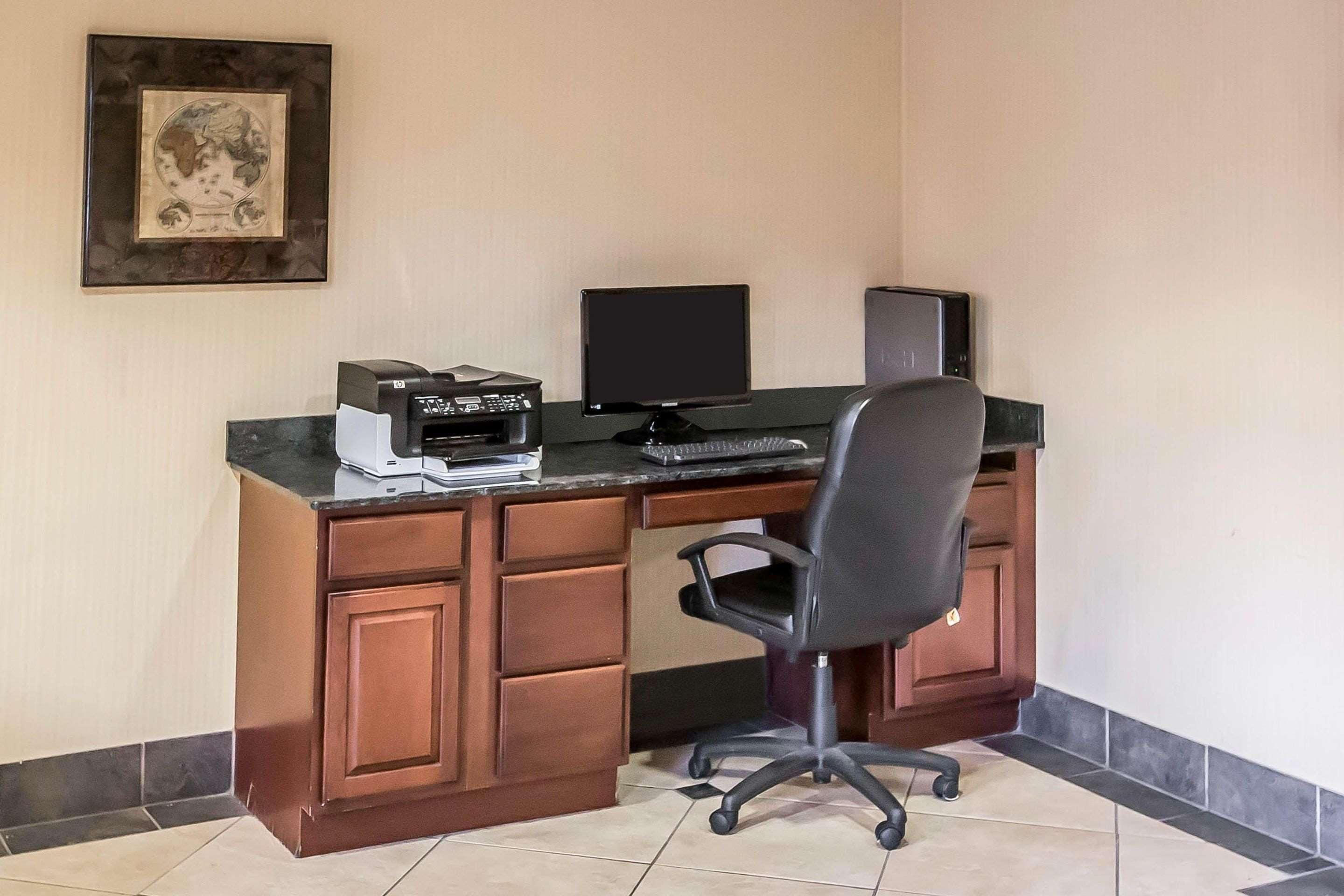 A desk with a computer, printer, and chair in a room with tiled flooring and wooden cabinetry.