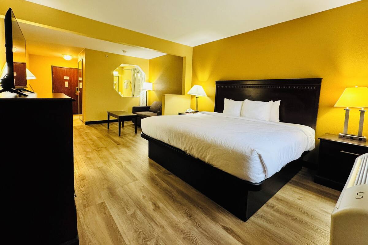 Una habitación de hotel con una cama grande, mesitas de noche, un escritorio y un espejo.
