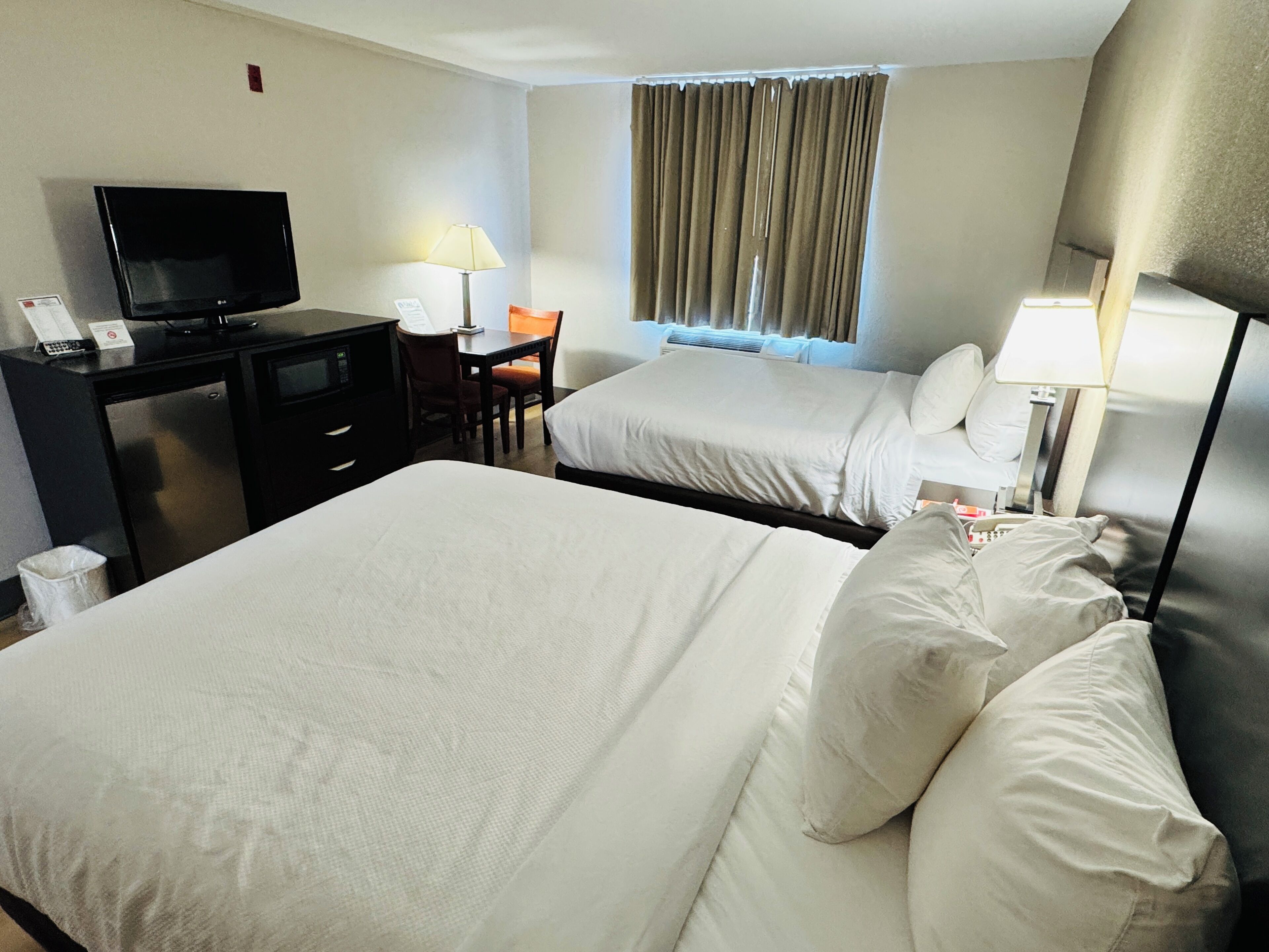 A hotel room with two beds, a desk with a television, a chair, and a window with curtains.