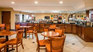 A hotel lobby with wooden tables and chairs, a coffee bar with various appliances, and a tiled floor.