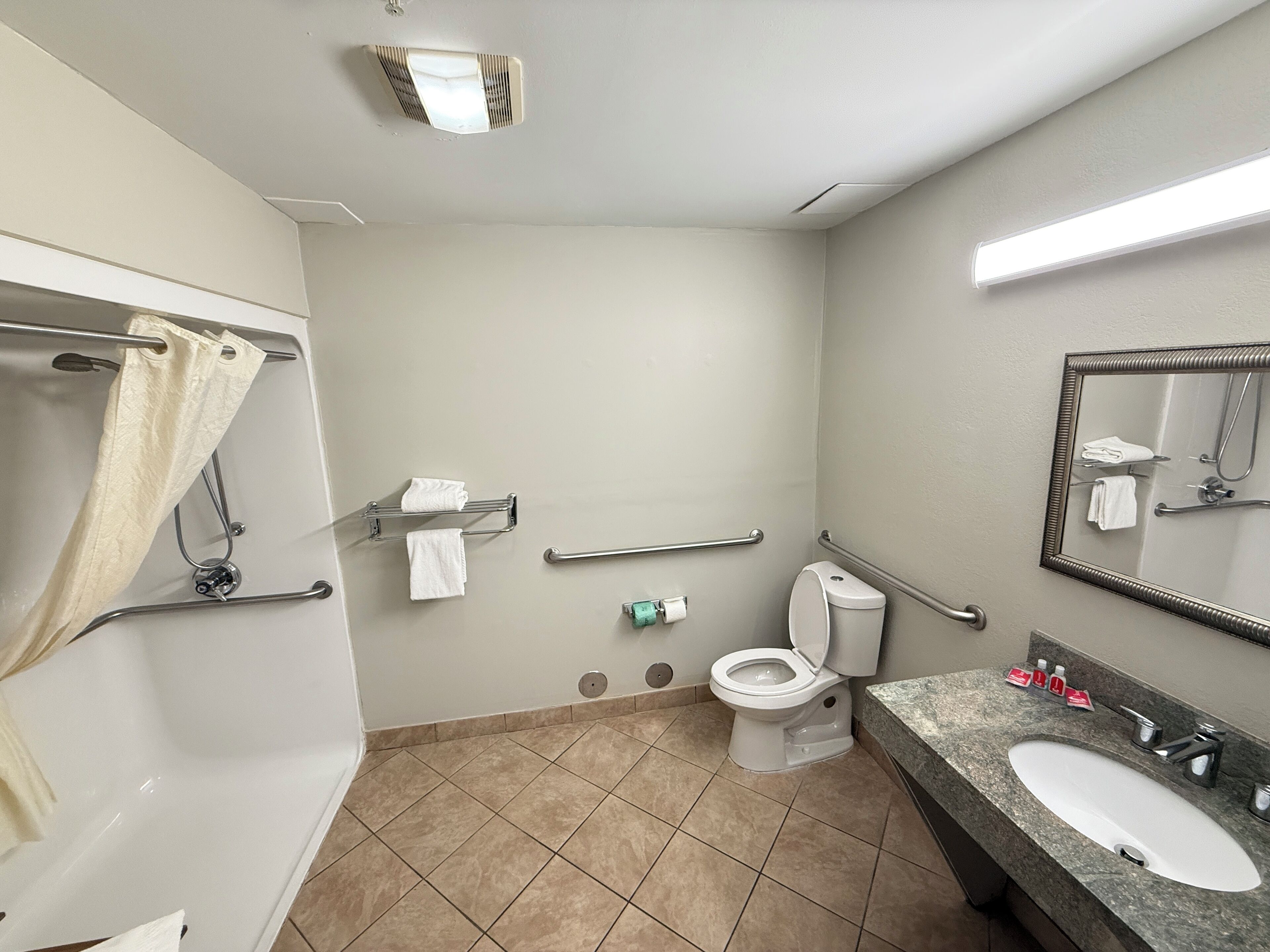 Un baño con inodoro, lavamanos, espejo, toallero y zona de ducha.