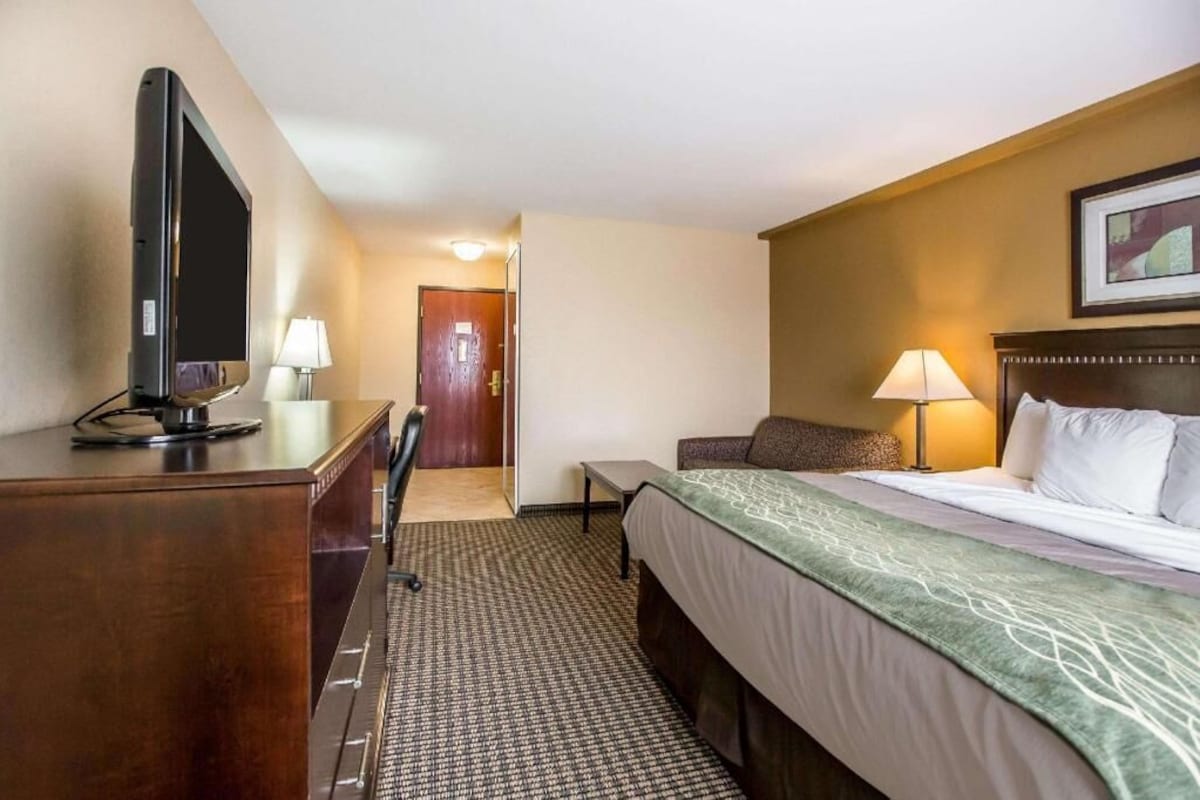 Een hotelkamer met een bed, bureau, televisie en een lamp.