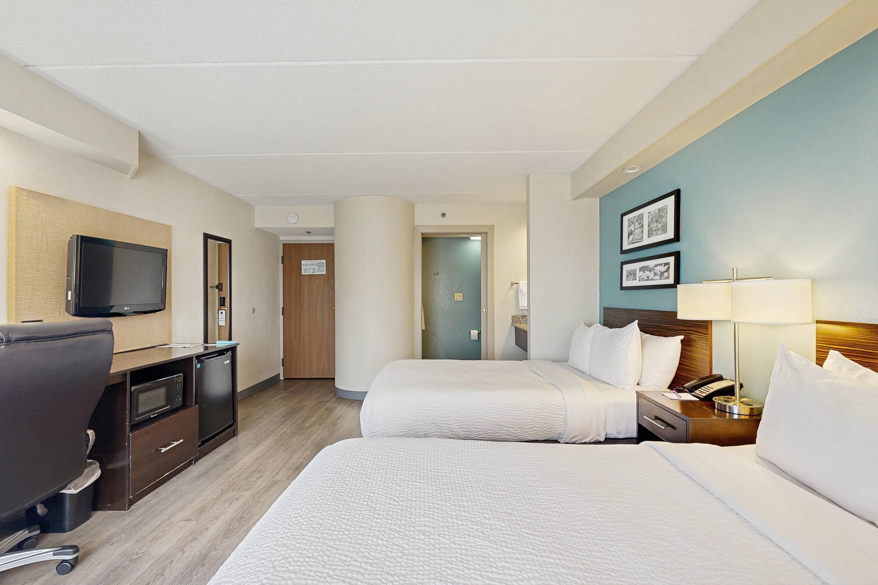 Habitación de hotel con dos camas, un escritorio, un televisor, un microondas y un refrigerador pequeño.