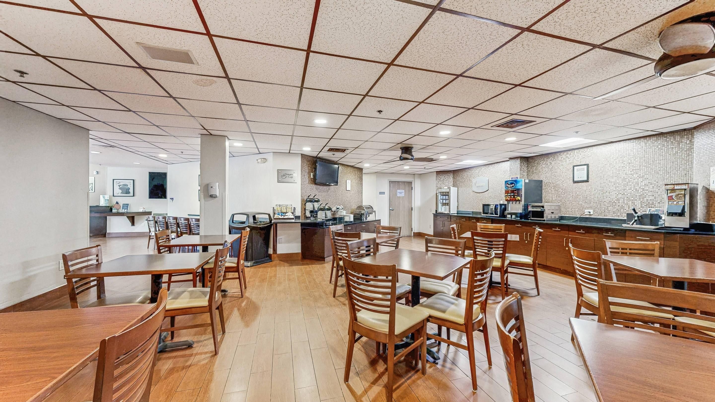 A spacious dining area with multiple tables and chairs, a kitchen area with appliances, and a tiled ceiling.
