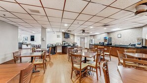 A spacious dining area with multiple tables and chairs, a kitchen area with appliances, and a tiled ceiling. - Sleep Inn & Suites Buffalo Airport (Buffalo)