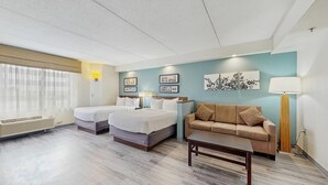 Una habitación de hotel con dos camas, un sofá, una mesa y una lámpara.
