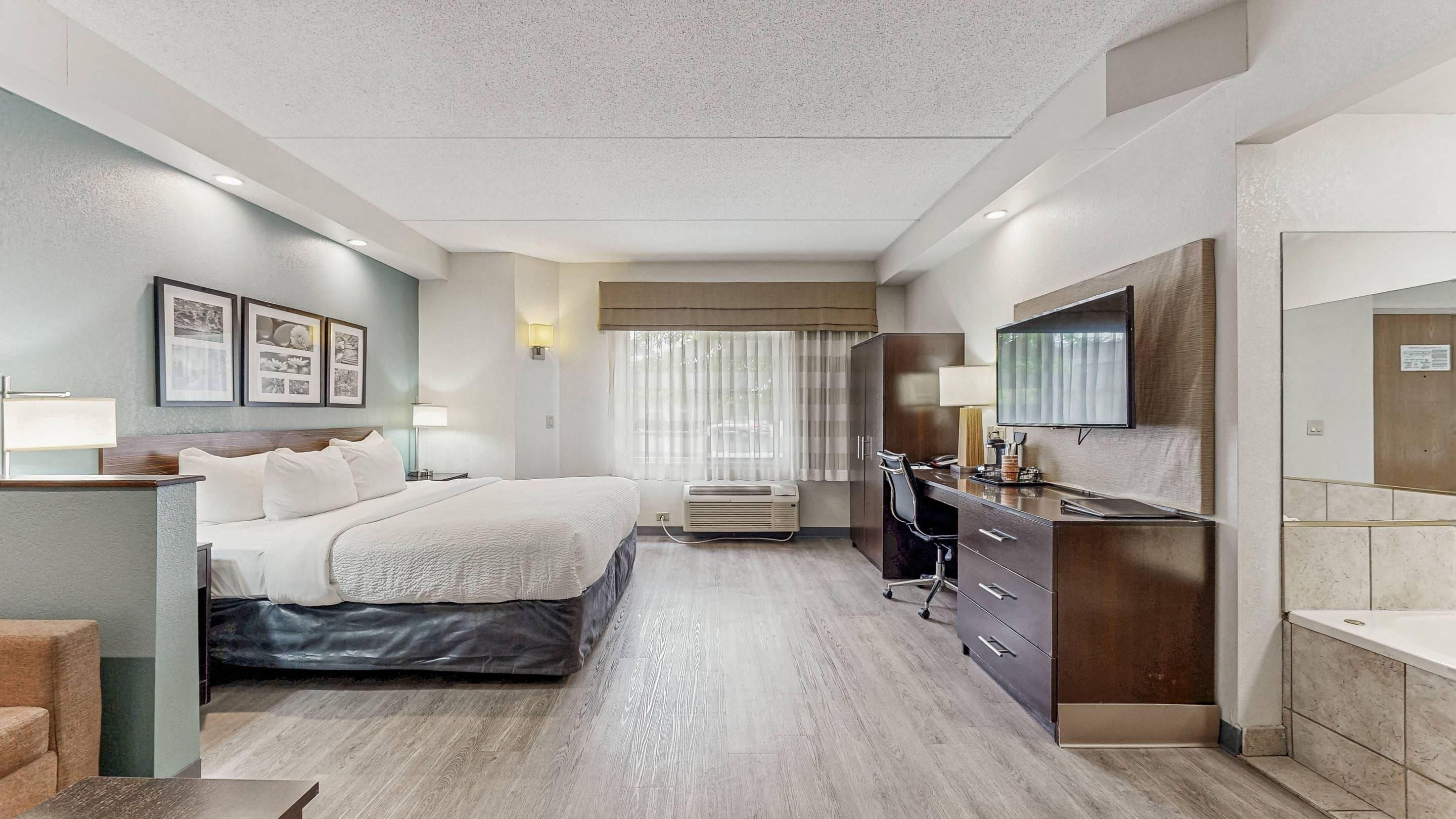 A hotel room with a bed, desk, chair, and a TV.
