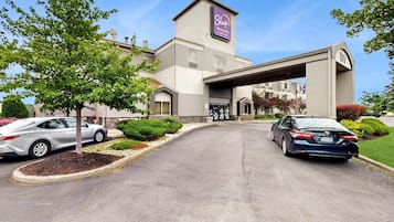 Un hotel Sleep Inn & Suites con un diseño moderno, que destaca por su entrada principal y un estacionamiento con dos coches.