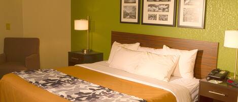 A hotel room with a bed, a chair, a nightstand with a lamp, and three framed pictures on the wall.