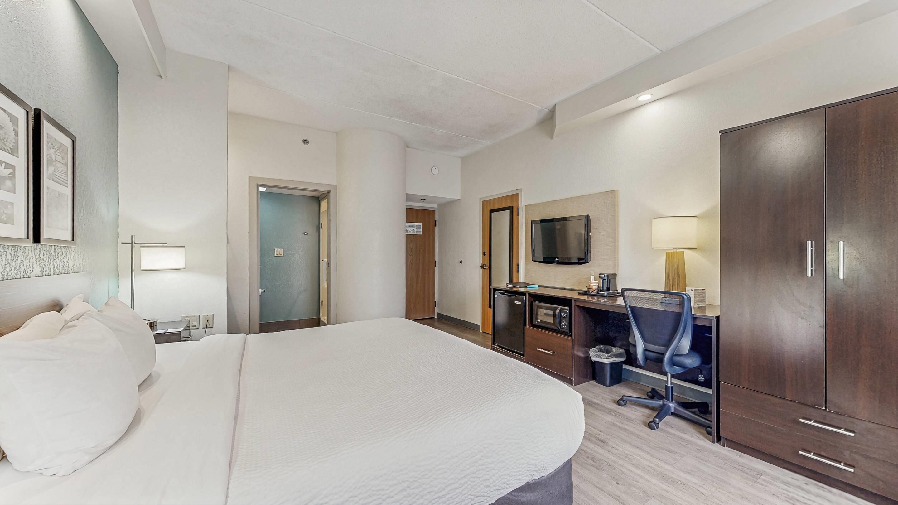 A hotel room with a large bed, a desk with a computer, a TV, and a wardrobe.