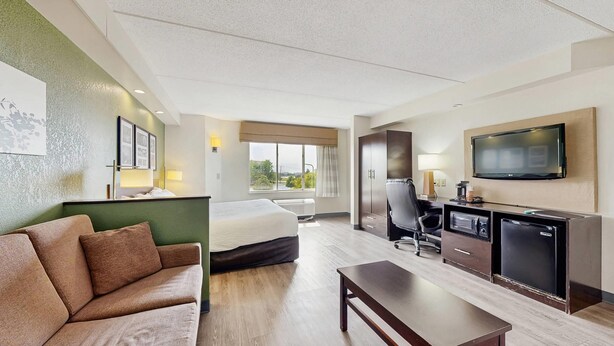 Habitación de hotel con cama, sofá, escritorio con silla, televisor y minibar.