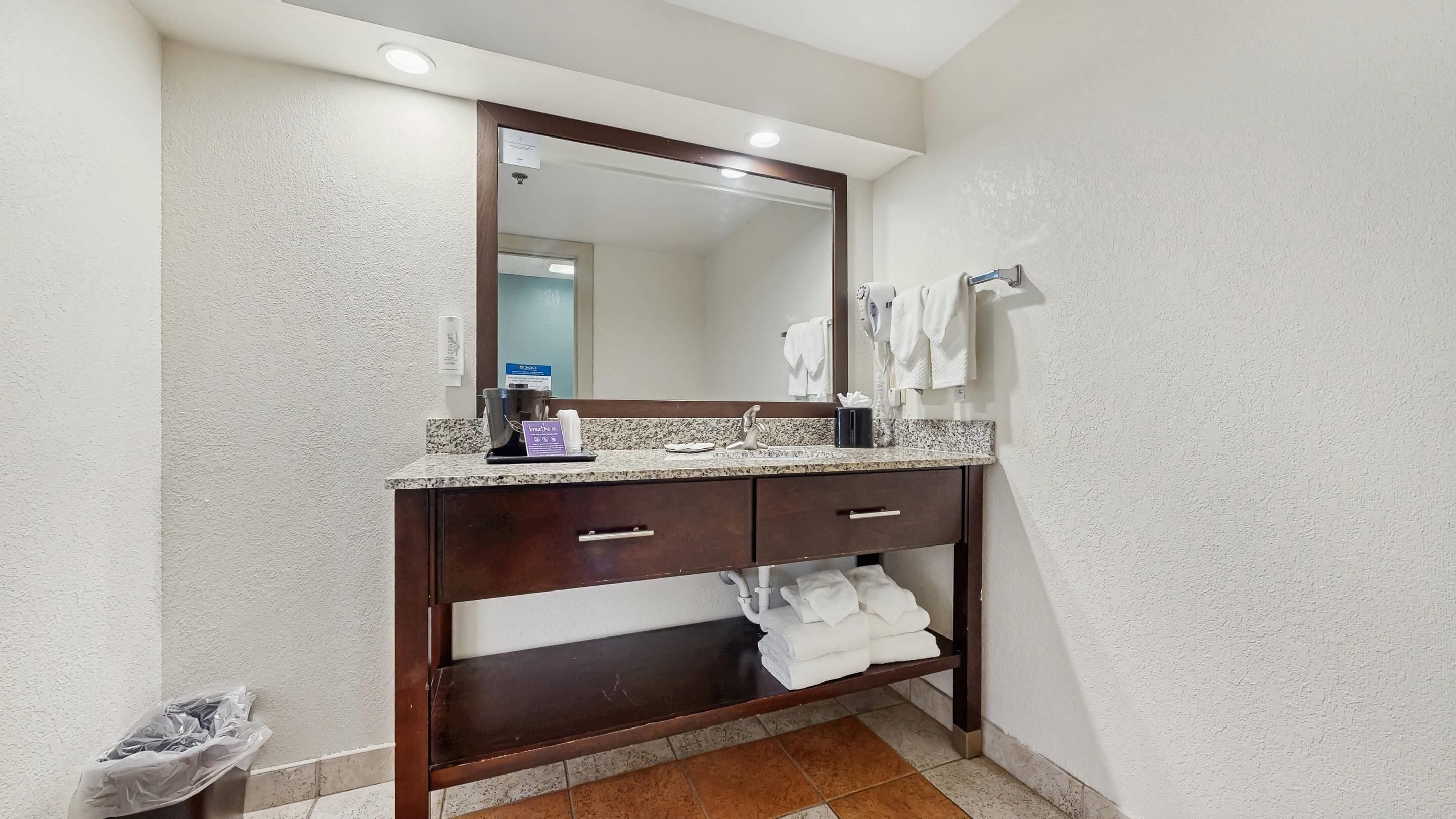 Une salle de bain avec un comptoir en granit, un meuble-lavabo en bois foncé, un miroir et un porte-serviettes.