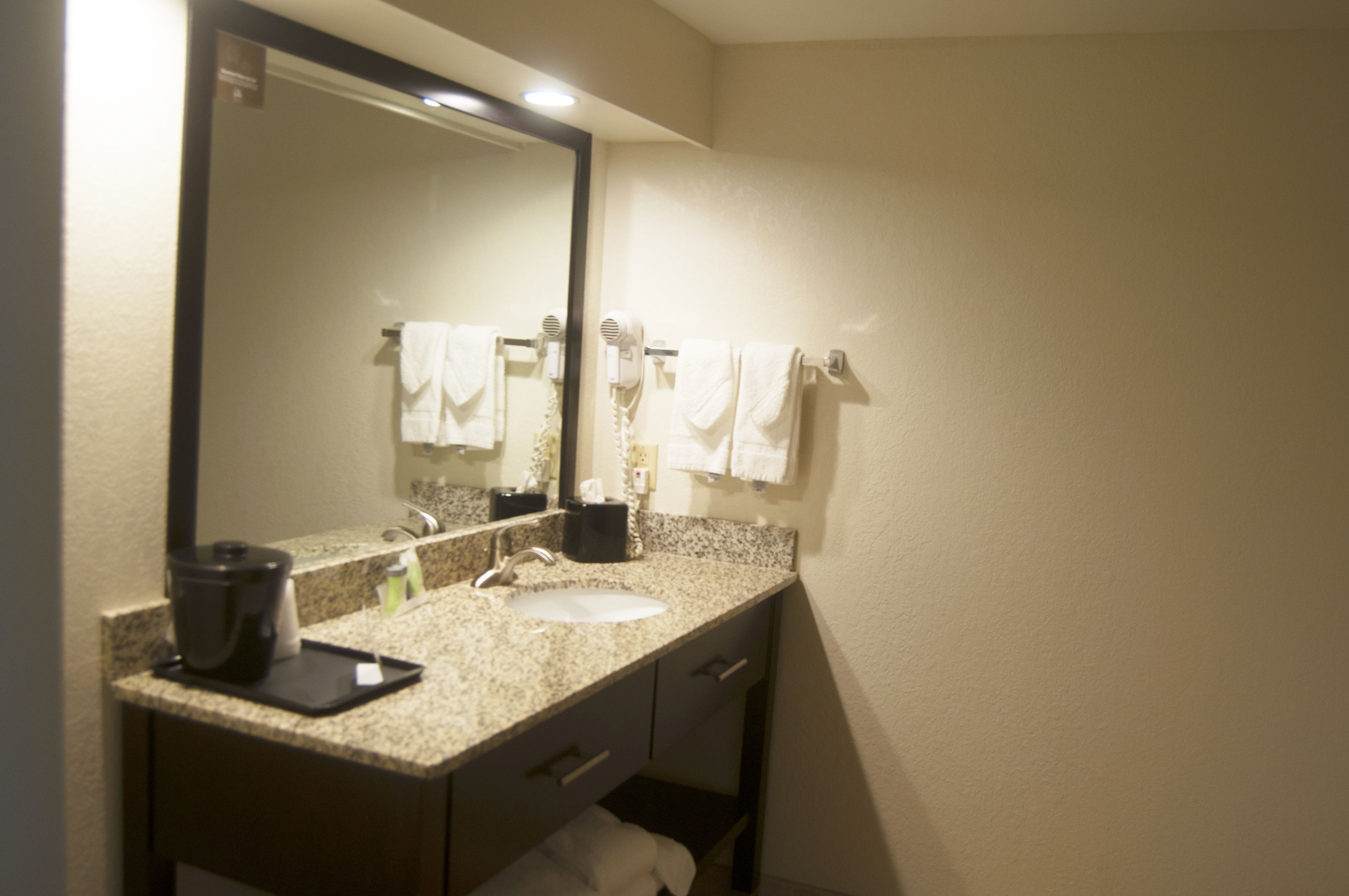 Un baño con encimera de granito, lavabo, espejo y secador de pelo.