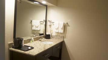 Un baño con encimera de granito, lavabo, espejo y secador de pelo.