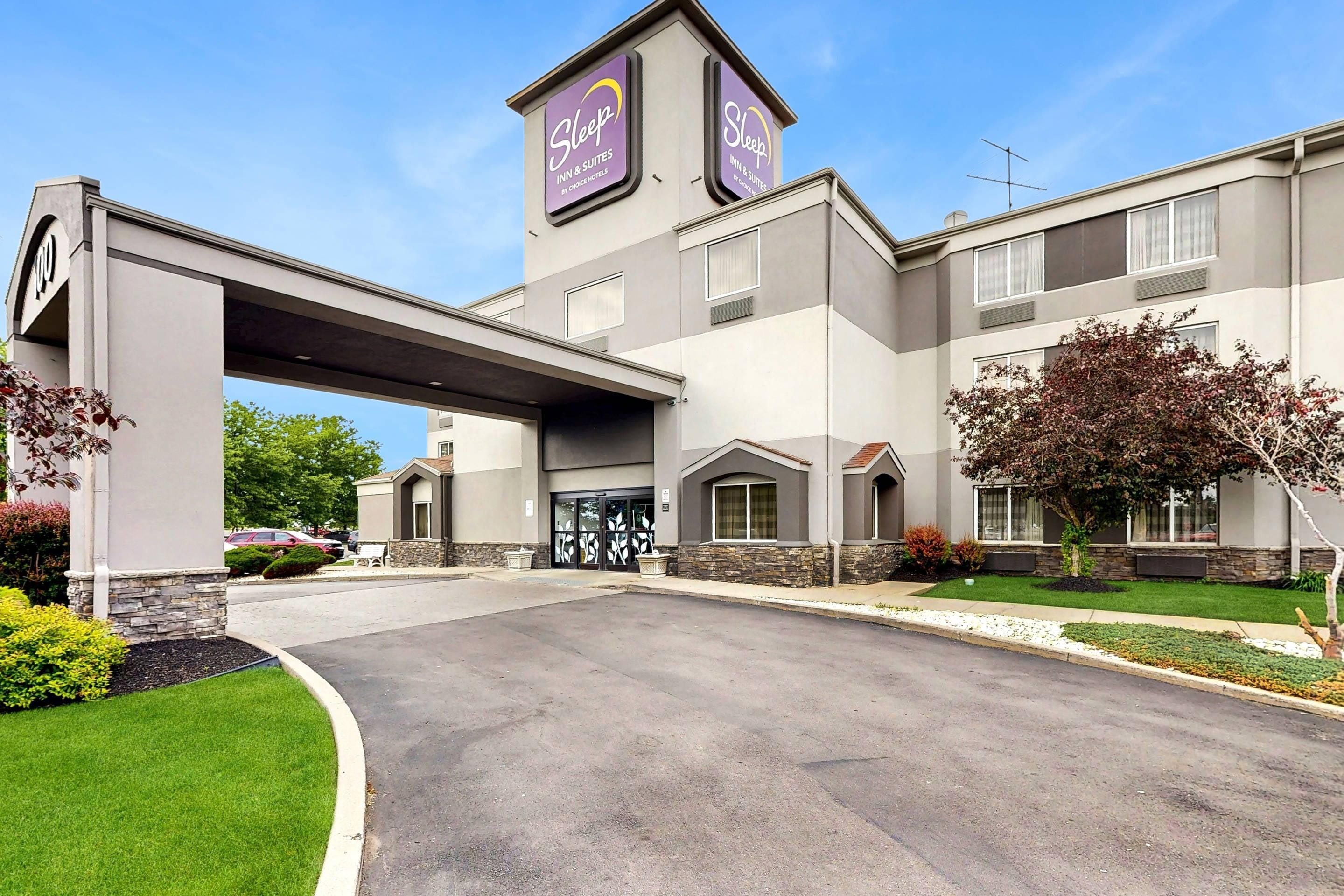 Un Sleep Inn & Suites de Choice Hotels con un diseño moderno, que cuenta con una entrada central, un pasillo cubierto y un área de estacionamiento.