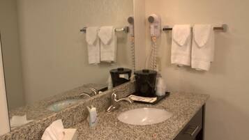 A bathroom with a granite countertop, a sink, a mirror, a hairdryer, and a towel rack.