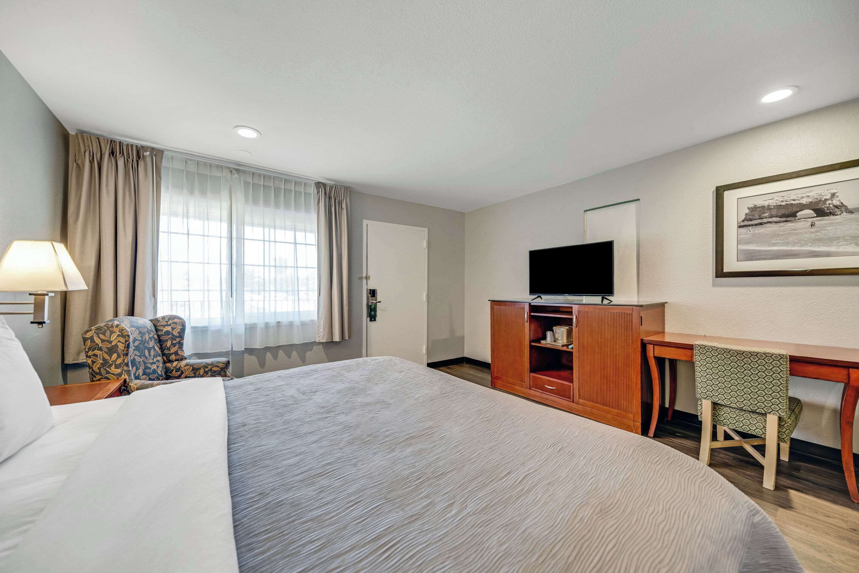 A hotel room with a large bed, a desk with a chair, a television, and a window with curtains.