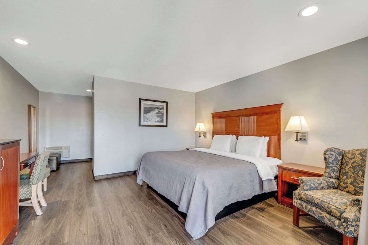 Habitación de hotel con cama, mesitas de noche, una silla, un escritorio y un cuadro en la pared.