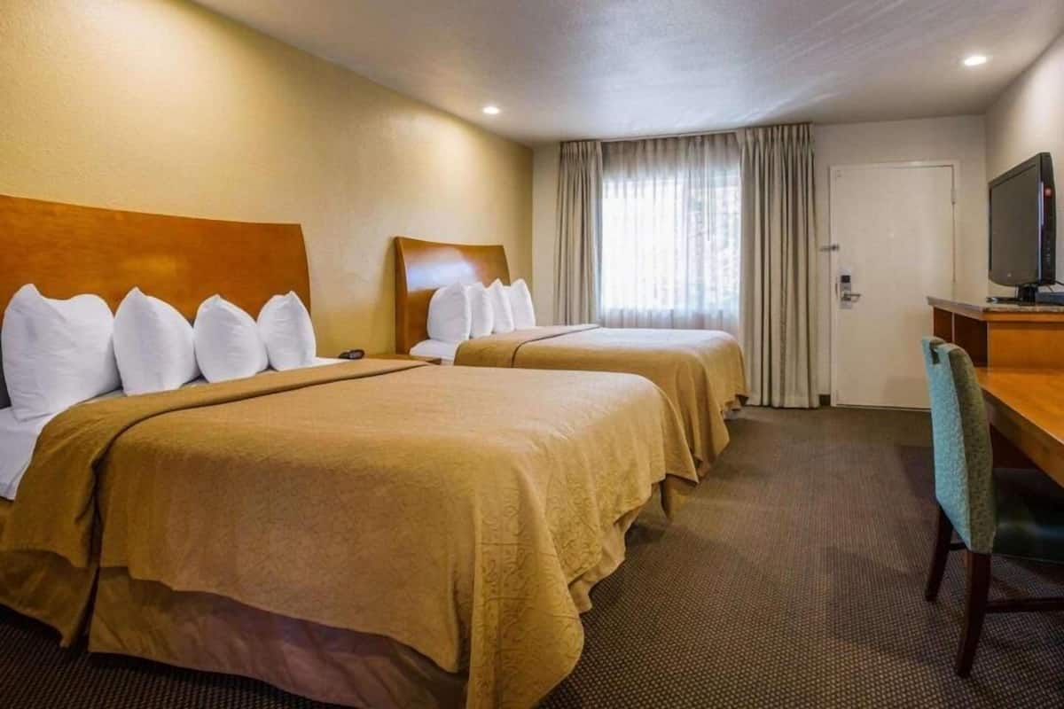 Habitación de hotel con dos camas, un escritorio y una televisión, y una puerta.