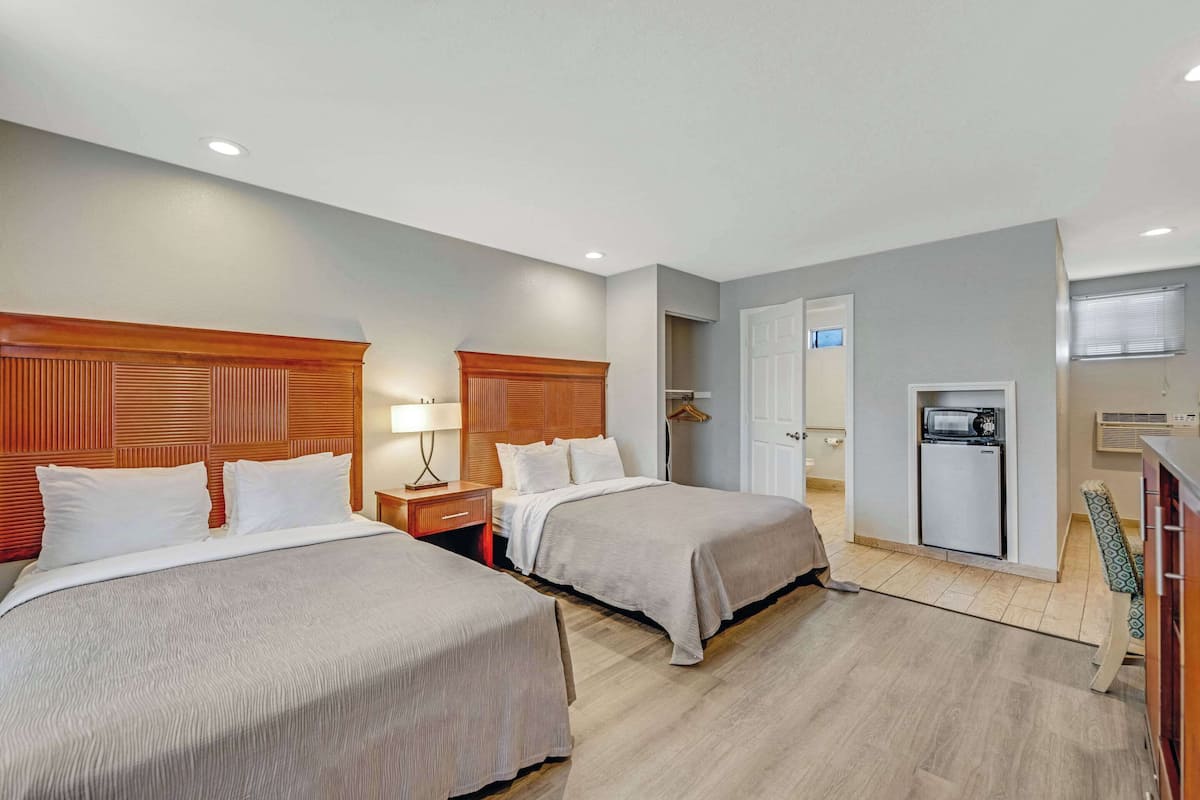 Habitación de hotel con dos camas, kitchenette, puerta que da a un baño y una pequeña zona de estar.
