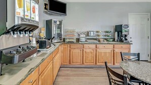 A kitchen with wooden cabinets, a granite countertop, a coffee machine, a toaster, and a television mounted on the wall. - Quality Inn Santa Cruz Downtown Area (Santa Cruz)