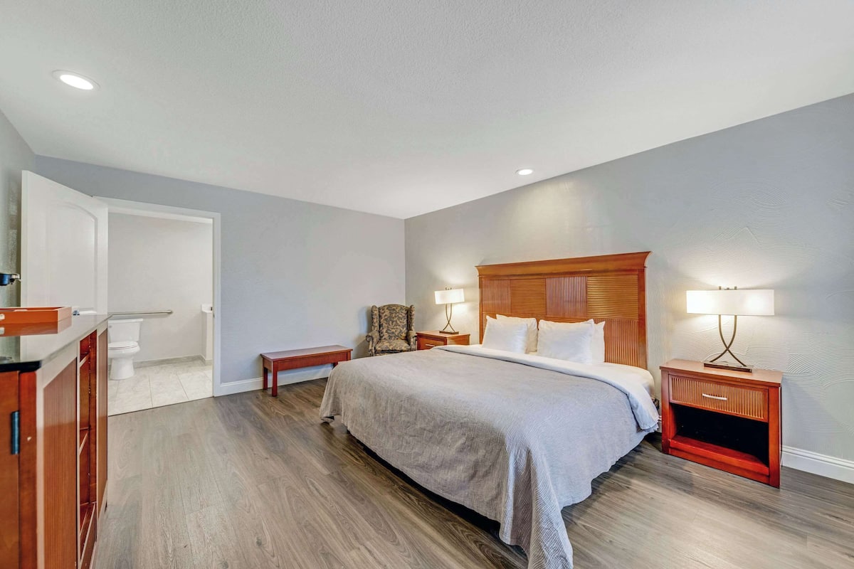Un dormitorio con una cama grande, cabecera de madera, dos mesitas de noche con lámparas, una silla y un armario de madera.