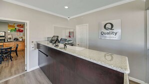 A hotel reception area with a counter, a sign indicating 'Quality by Choice Hotels', and a glimpse of a dining area with a table and chairs. - Quality Inn Santa Cruz Downtown Area (Santa Cruz)