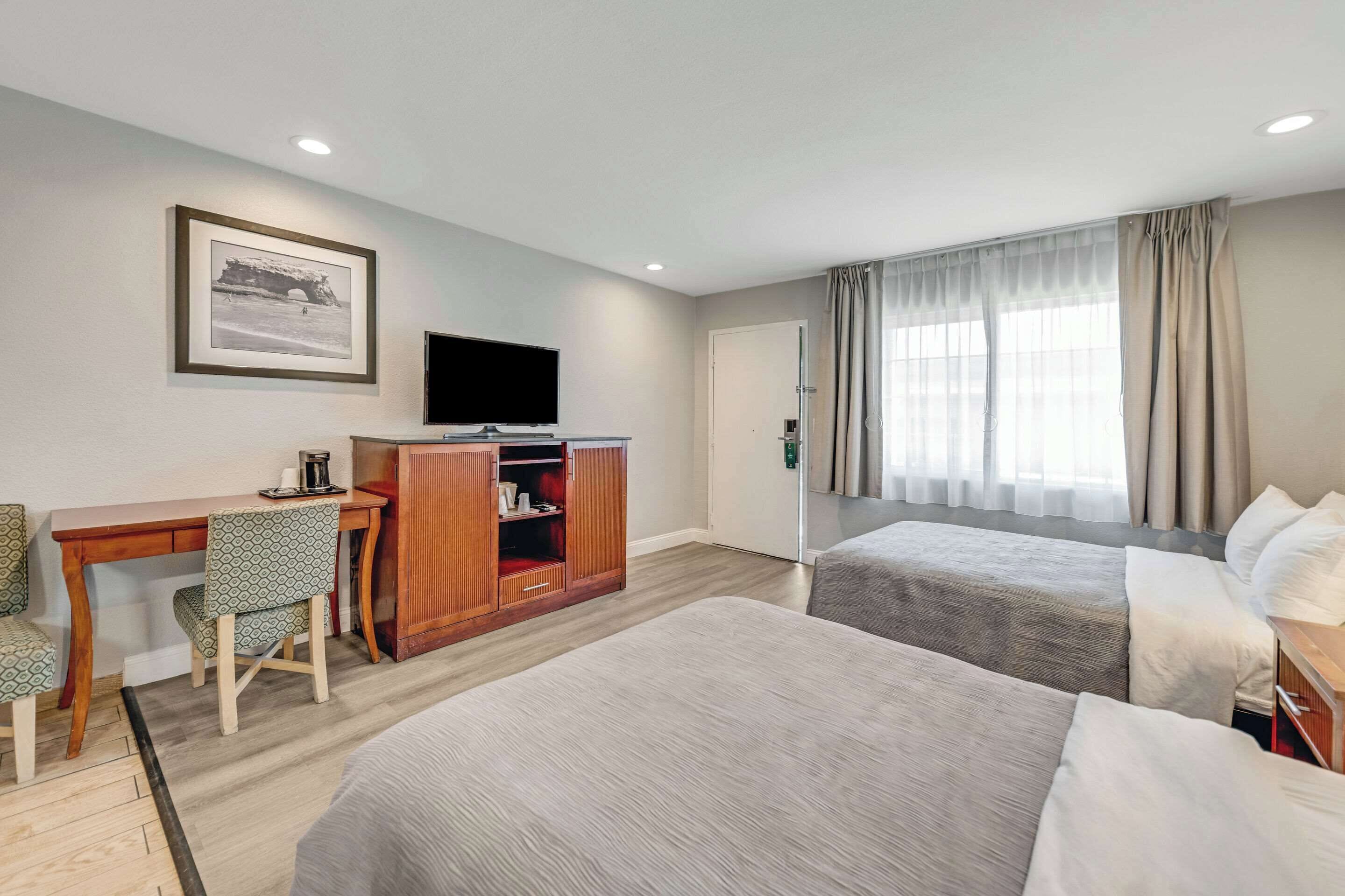 A hotel room with two beds, a desk with a chair, a television, and a wardrobe.