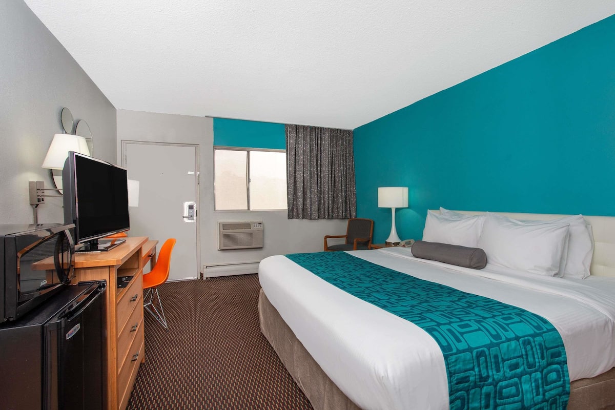A hotel room with a bed, a desk with a computer, a chair, and a TV.