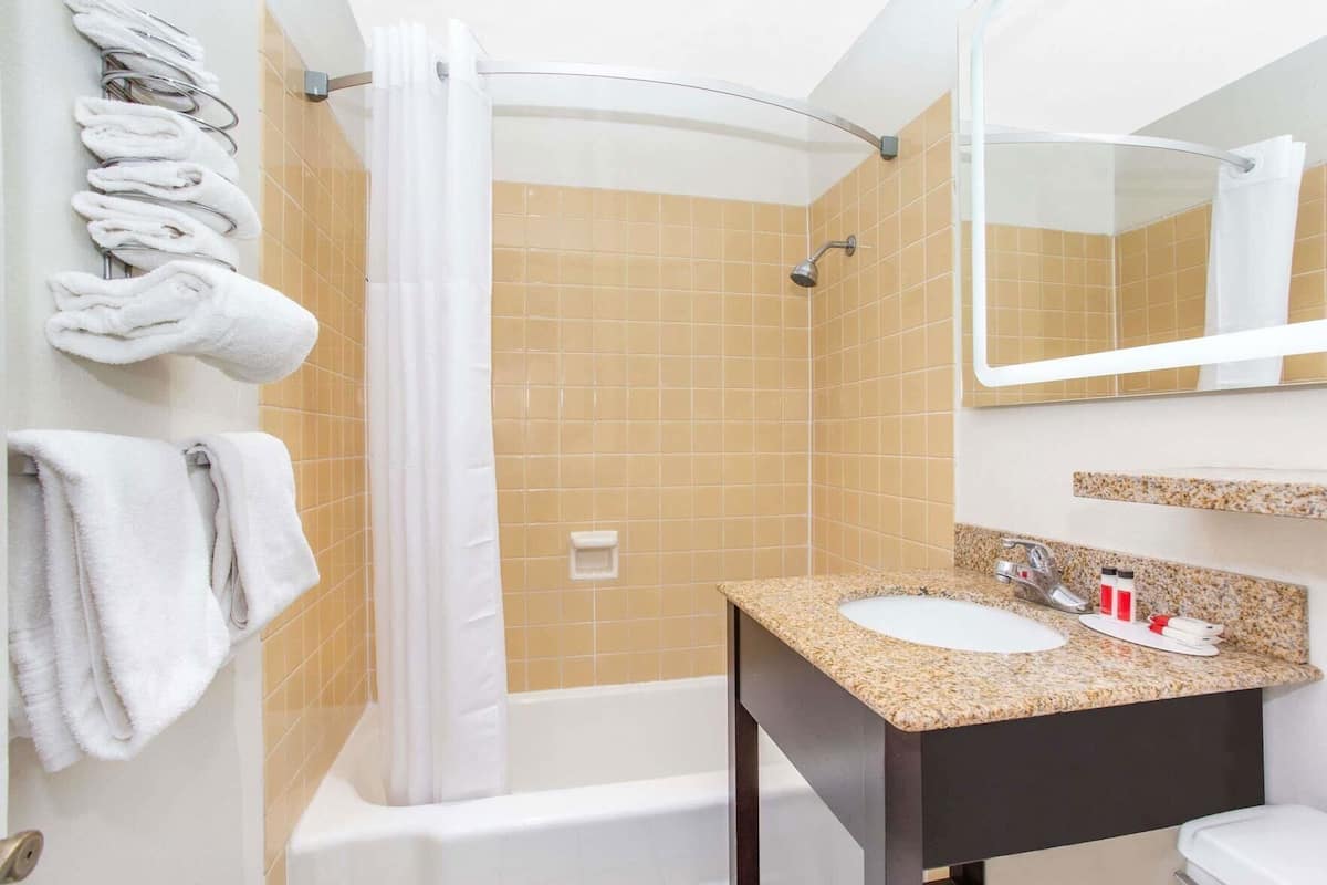 A bathroom with a bathtub, shower, white towels, a sink with a granite countertop, and a mirror.