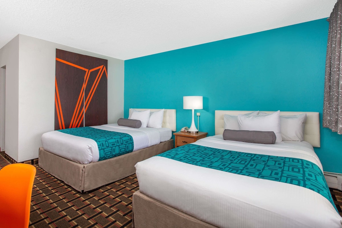 A hotel room with two beds, a patterned floor, and a teal accent wall.
