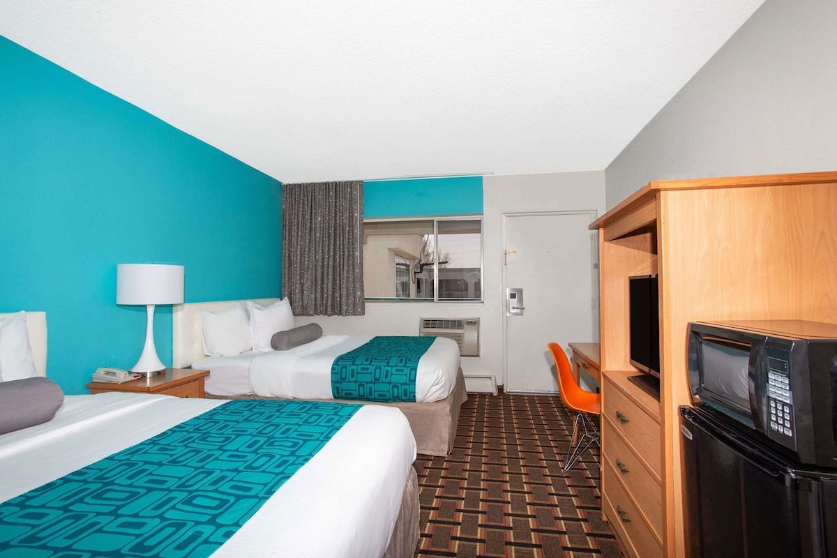 A hotel room with two beds, a desk with a TV, a microwave, and a bathroom door.