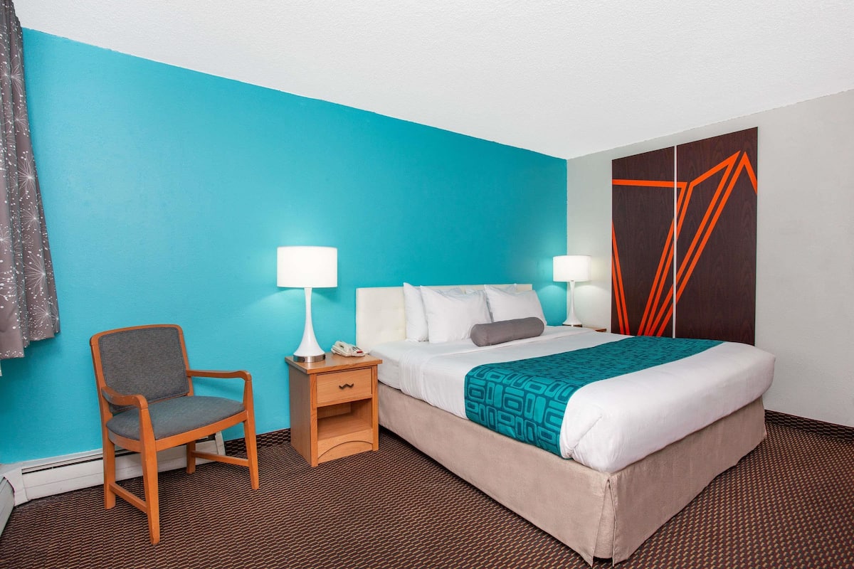 A hotel room with a bed, a chair, a nightstand, and a wall with geometric patterns.