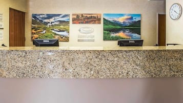 A hotel reception desk with three framed landscape paintings, a clock, and two Dell computers.