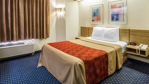 Ein Hotelzimmer mit Bett, Nachttisch, Lampe und einem Fenster mit Vorhängen.