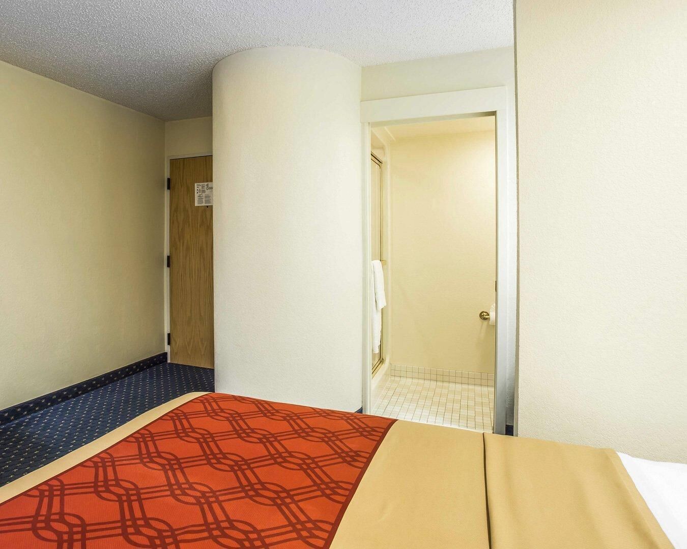 Une chambre d’hôtel avec un lit, une porte en bois et une salle de bain visible à travers une porte ouverte.