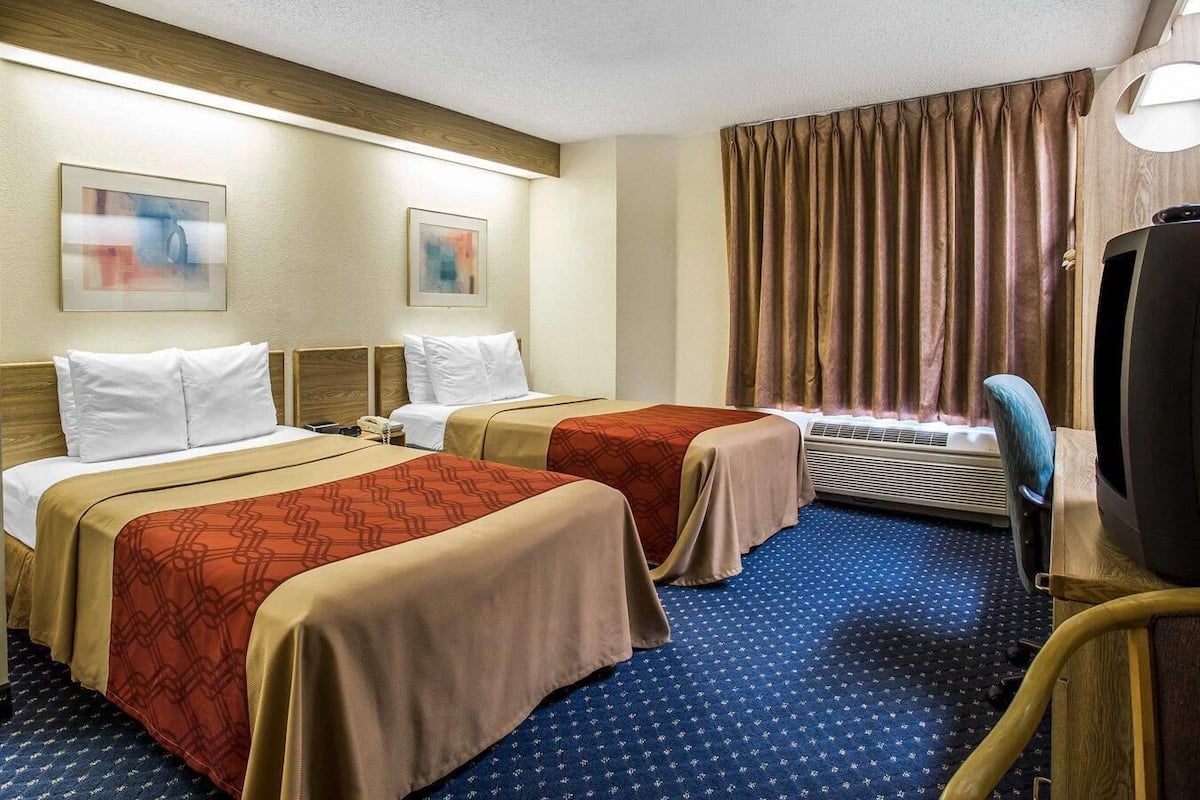 A hotel room with two beds, a desk with a television, and a window with curtains.