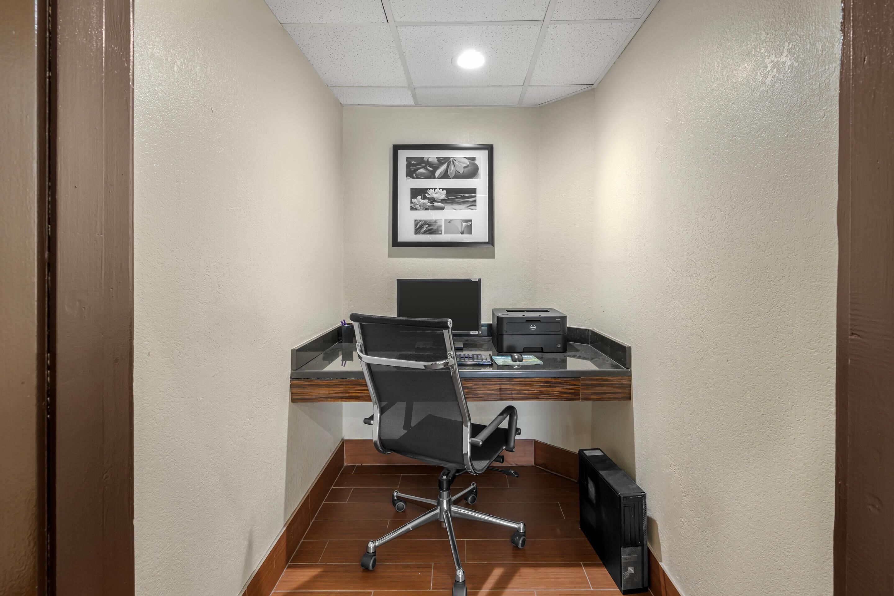 A small office with a desk, chair, computer, printer, and a framed picture on the wall.