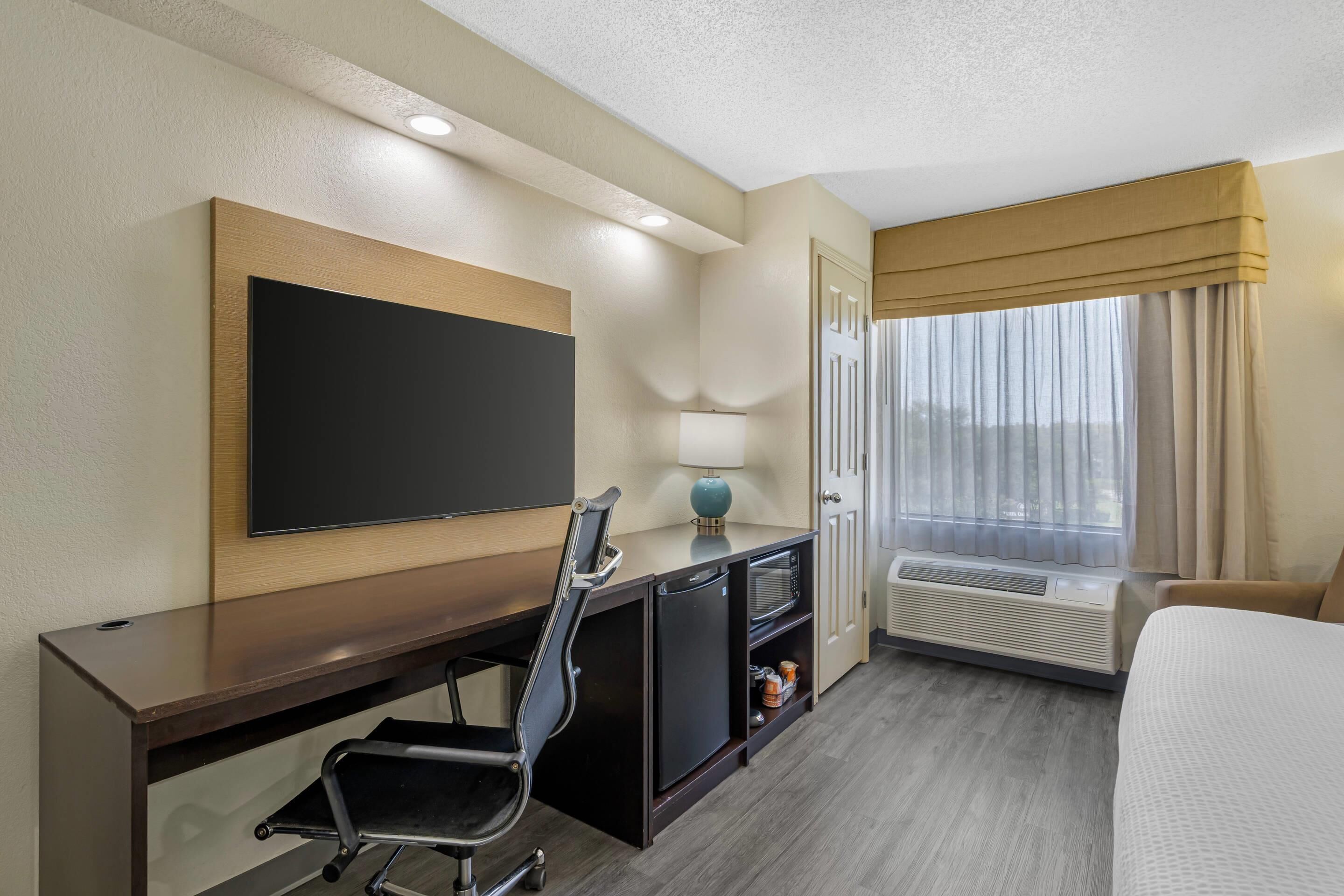 Une chambre d’hôtel équipée d’un téléviseur à écran plat fixé au mur, d’un bureau avec une chaise, d’une table de chevet avec une lampe, d’un climatiseur et d’un lit.