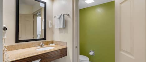 A bathroom with a beige vanity, a large mirror, a white sink, and a green accent wall.