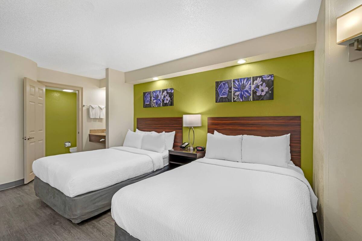 Ein Hotelzimmer mit zwei Betten, einer grünen Akzentwand und einem Holzkopfende.