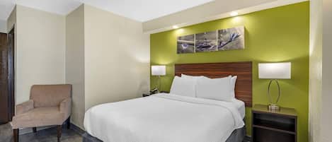 Une chambre d’hôtel avec un lit, une chaise et une table de chevet avec une lampe.