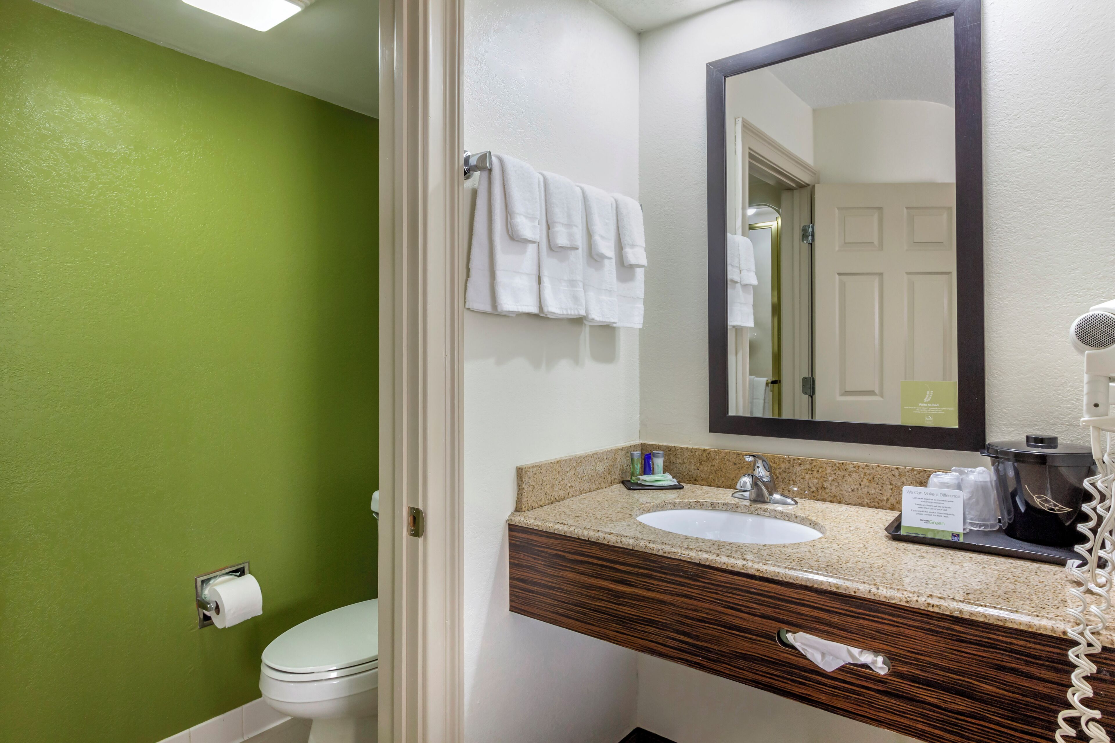 A bathroom with a green wall, white toilet, and a sink with a mirror above it.