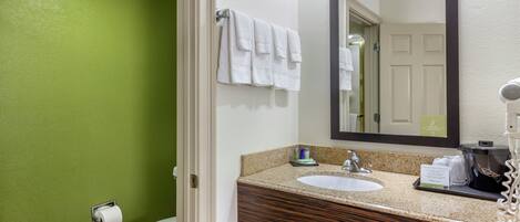 A bathroom with a green wall, white toilet, and a sink with a mirror above it.