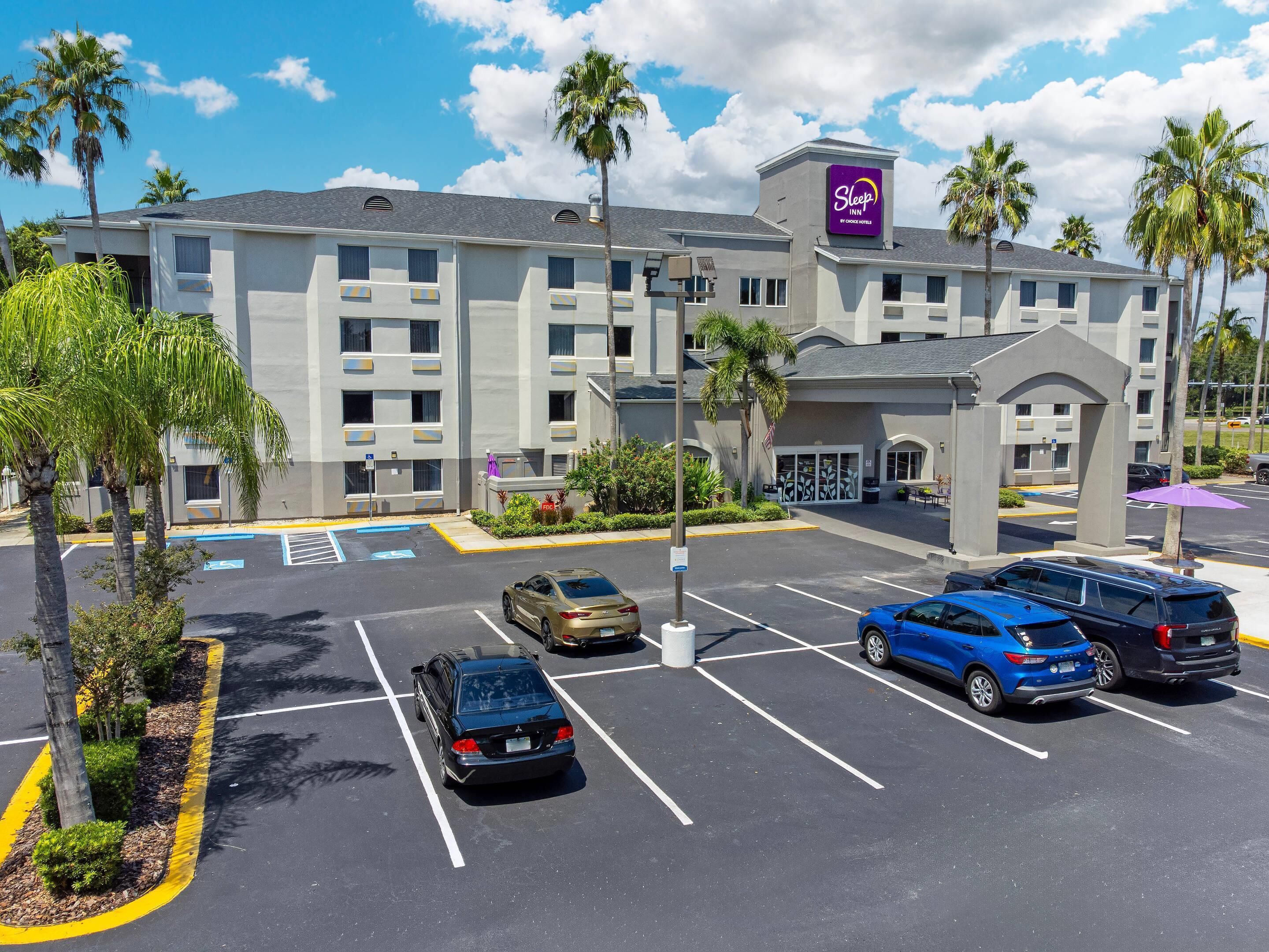 Un hotel con estacionamiento, palmeras y un letrero Sleep by Choice Inn.