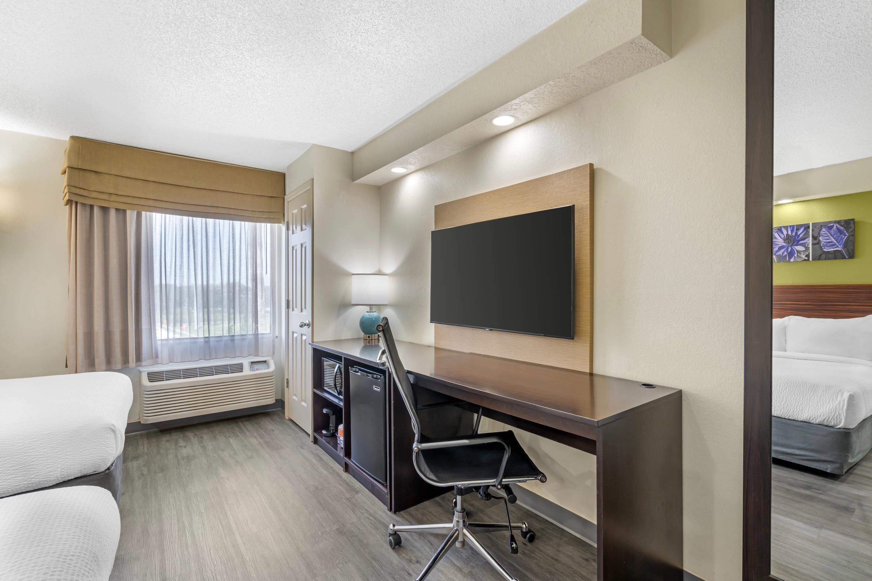 Une chambre d’hôtel comprenant un lit, un bureau avec une chaise, un téléviseur à écran plat, un minibar et une fenêtre avec des rideaux.