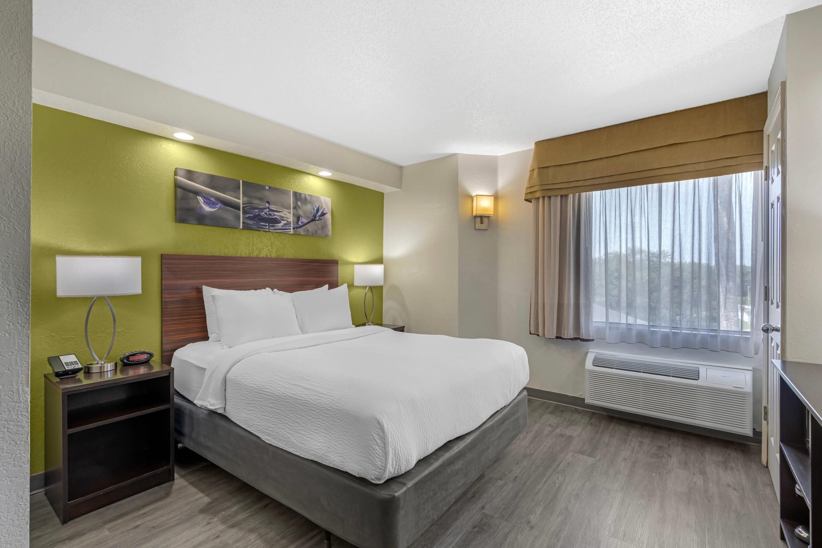 A hotel room with a bed, bedside lamps, a phone, a heater, and artwork on the wall.