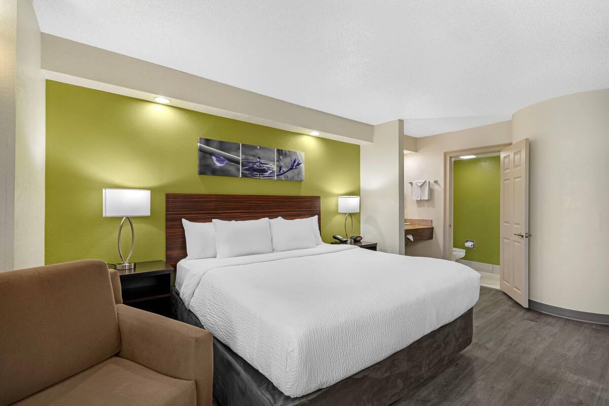 Ein Hotelzimmer mit einem großen Bett, zwei Nachttischen mit Lampen, einer grünen Akzentwand und einem Holzkopfteil.