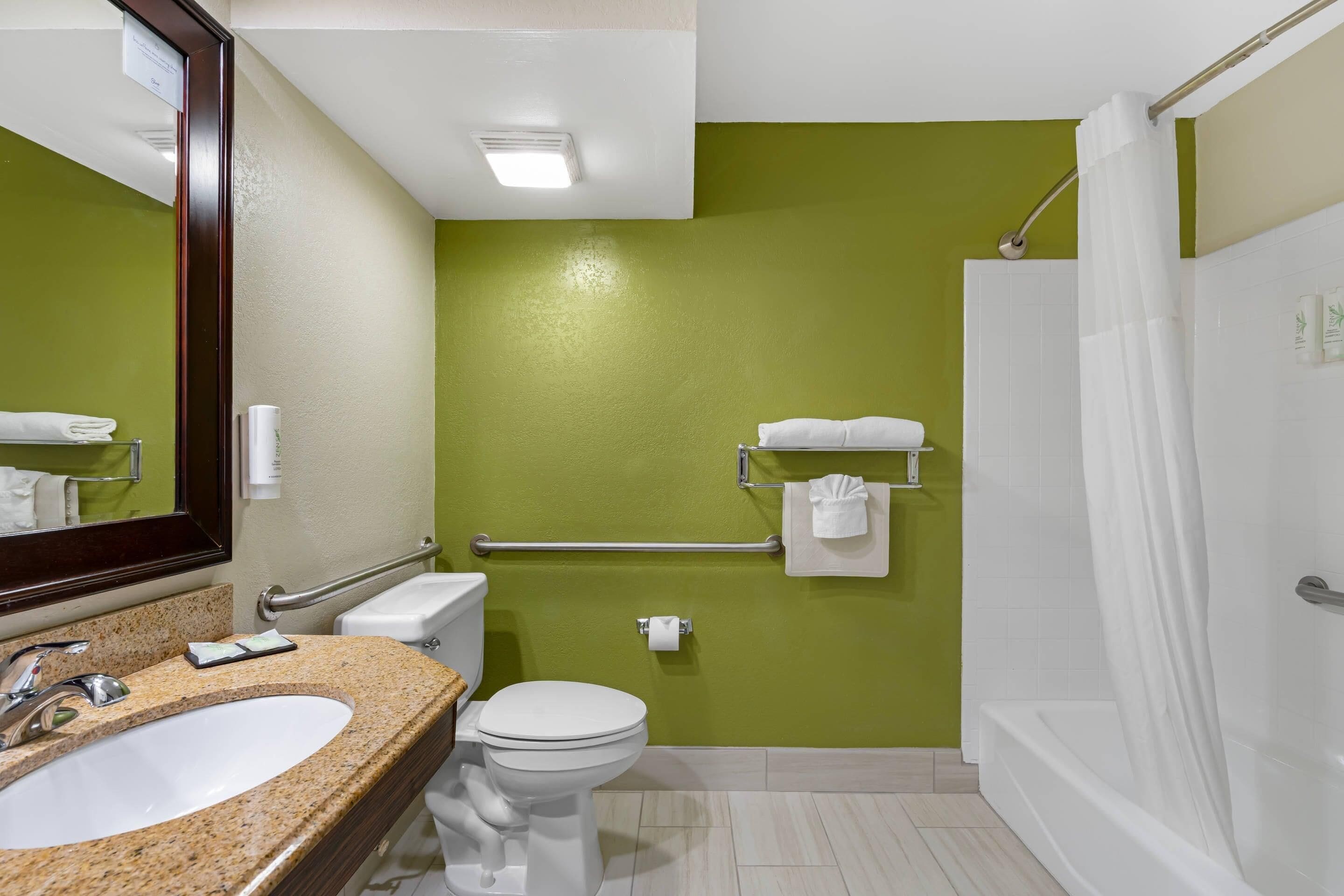 A bathroom with a granite sink, white toilet, and a shower with a white curtain.