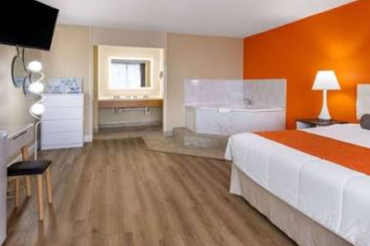 A hotel room with a bed, a desk, a chair, a lamp, and a bathroom visible through an open door.